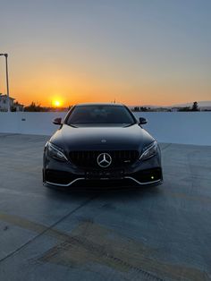 the front end of a black mercedes s - class coupe parked in a parking lot at sunset