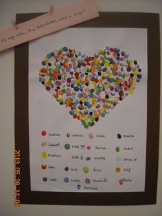 a heart made out of many different colored buttons on a piece of paper next to a brown frame