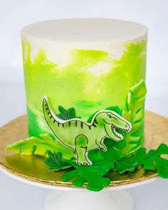 a green and white cake with a dinosaur decoration on the top is sitting on a gold plate