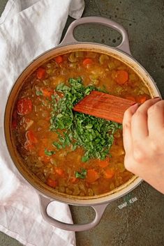 a person stirring a pot of soup with a wooden spoon on the side and napkins next to it