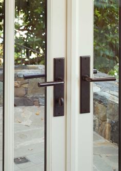 an open door with black handles and glass panels on the outside wall, in front of a stone patio area