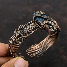 a close up of a person holding a metal bracelet with an intricate design on it