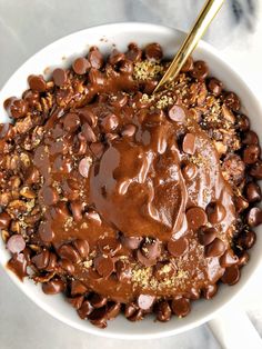 a bowl filled with chocolate and nuts on top of a marble countertop next to a spoon