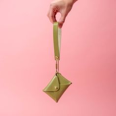 a person's hand holding an origami purse on a pink background,