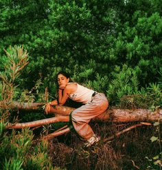 a young man leaning on a fallen tree in the middle of some bushes and trees