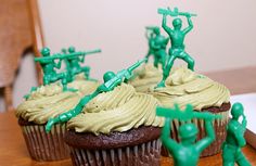 cupcakes with green frosting and toy army men on top are sitting on a table