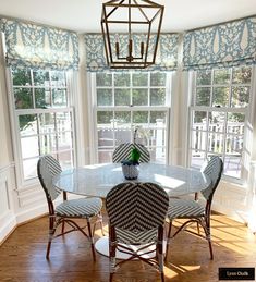 a dinning room table with four chairs and a vase on the table in front of two windows