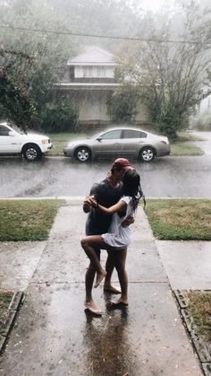 two people are hugging on the sidewalk in the rain, with cars parked behind them