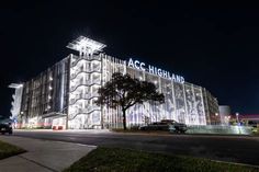 an illuminated building at night with cars parked on the street in front and behind it