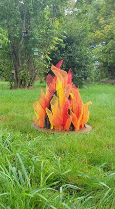 Campfire of red, orange and yellow pretend flames with logs arranged tee-pee style on green grass yard. Pretend Campfire, Fake Campfire, Percy Jackson Party, Camp Vbs, Fire Crafts, Fake Fire, Glowing Embers, Indoor Camping, Vbs Themes