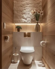 a white toilet sitting inside of a bathroom next to a vase with flowers on it