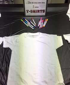 t - shirts are laid out on top of a black and white bed spread with colored crayons