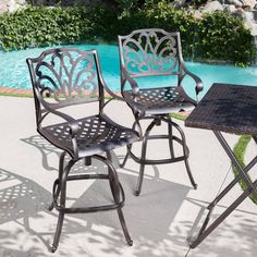 two wrought iron bar stools next to a swimming pool with a table and chair