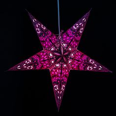 a large pink star hanging from a string on a black background with the lights turned on