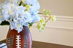 a football vase filled with blue flowers on top of a wooden table next to a striped napkin