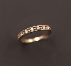 a gold wedding band with small diamonds on it's sides, sitting on a black surface