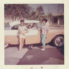 two women standing next to an old car with three children in the back seat,