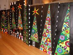 a row of christmas trees painted on black canvases with white and green stripes, sitting on a hard wood floor