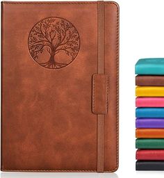 a brown leather journal with colored books next to it and an image of a tree on the cover