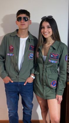 two people standing next to each other in front of a wall wearing green jackets and sunglasses