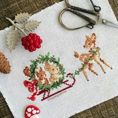 a cross - stitch christmas scene with deers, berries and pine cones on a table