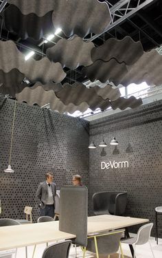 two men are standing in front of the devom booth at an event with chairs and tables