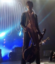 a man standing on stage with his guitar in front of him and lights behind him