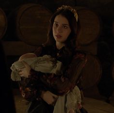 a woman holding a baby in her arms while standing next to some wine casks