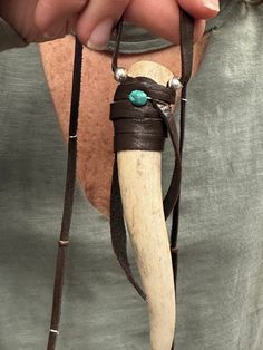 a person holding an animal's long horn in their right hand and wearing a leather bracelet with turquoise stones on it