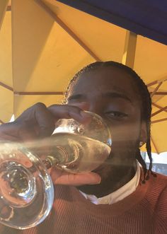 a man drinking from a wine glass in front of an umbrella with the sun shining on him