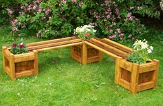 three wooden planters sitting on top of green grass next to bushes and flowers in them