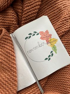 an open notebook with the word november written on it next to a knitted blanket