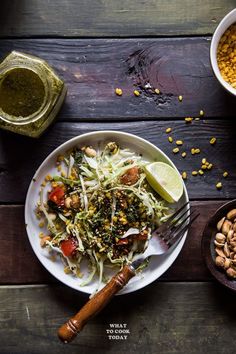 a white plate topped with salad next to two bowls filled with beans and limes