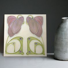 a white vase sitting on top of a table next to a ceramic wall art piece