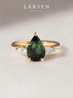 a pear shaped green and white diamond ring with three diamonds on the band, set in yellow gold