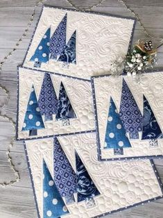 four quilted christmas trees are displayed on a tablecloth with blue and white designs