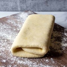 a rolled up dough sitting on top of a wooden cutting board covered in powdered sugar