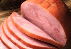 slices of ham are stacked on top of each other in front of some breads