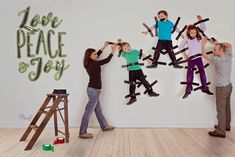 a group of people standing in front of a white wall with the words love peace and joy on it