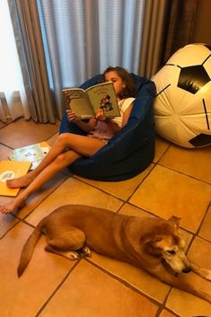 a woman sitting on a bean bag chair reading a book with her dog laying next to her