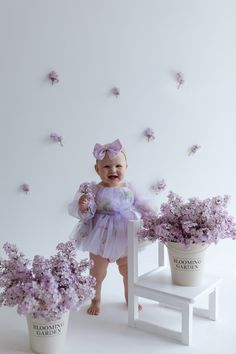 a baby girl standing next to some flowers