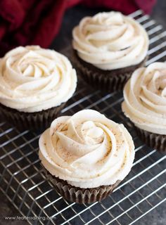 four cupcakes with white frosting on a cooling rack