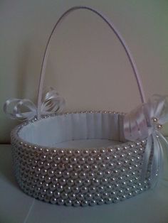 a white basket with pearls and bows on the handle is sitting on top of a table