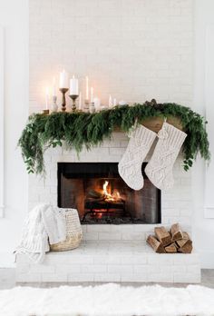 a white fireplace with stockings and candles on it's mantle, decorated for christmas