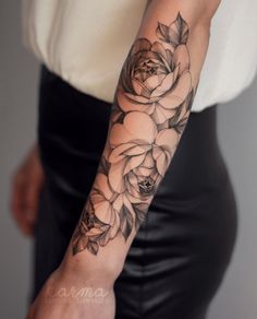 a woman's arm with black and white roses tattooed on the arm, in front of her