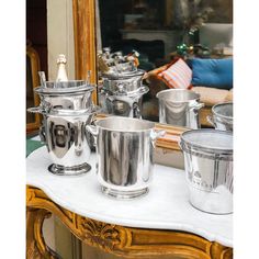 several silver cups sitting on top of a white table next to a mirror and couch