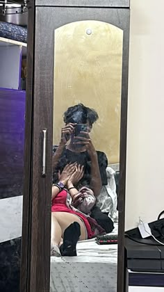 a woman taking a selfie in a mirror next to a man sitting on a bed