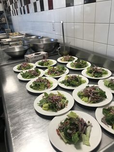 many plates with salad on them are lined up in a kitchen