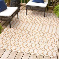 an outdoor area rug with two chairs and pillows on top of the floor, next to a wooden deck