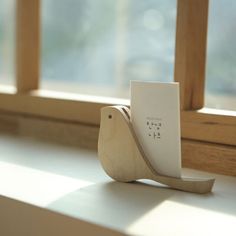 a wooden bird figurine sitting on top of a window sill next to a piece of paper